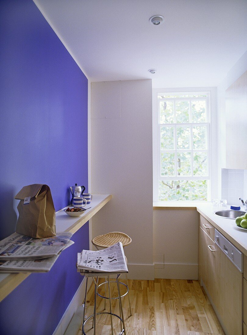 A detail of a modern kitchen with breakfast bar, blue feature wall, sink unit, wooden flooring,