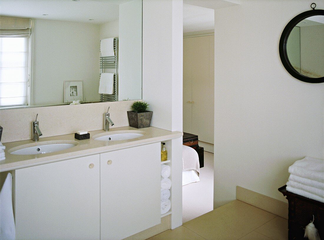A detail of a modern, neutral en suite bathroom, twin washbasins set in a storage cupboard unit