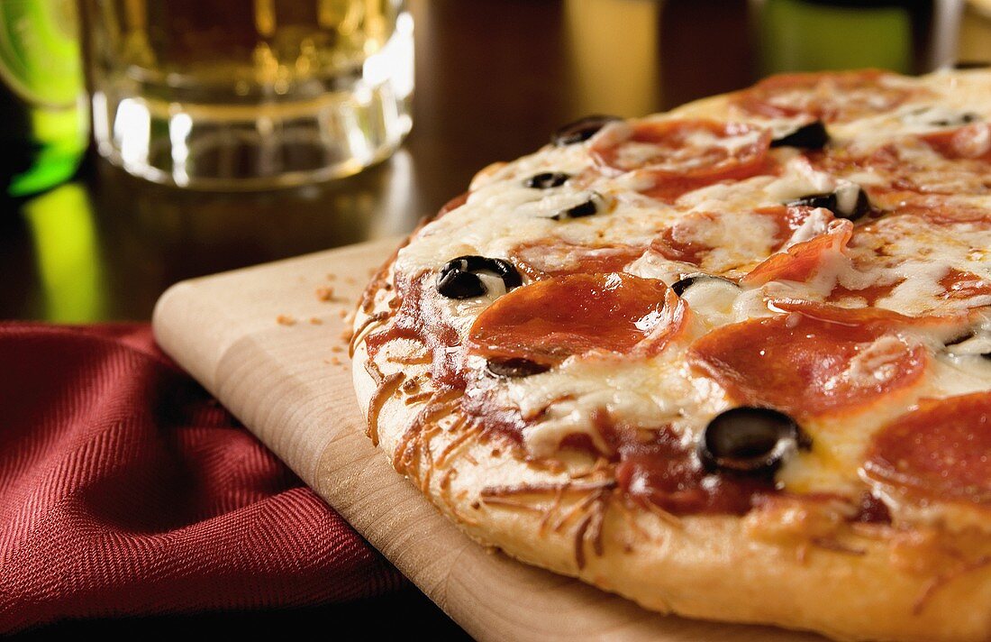 Eine Pizza mit Salami, Oliven und Käse auf einem Holzbrett