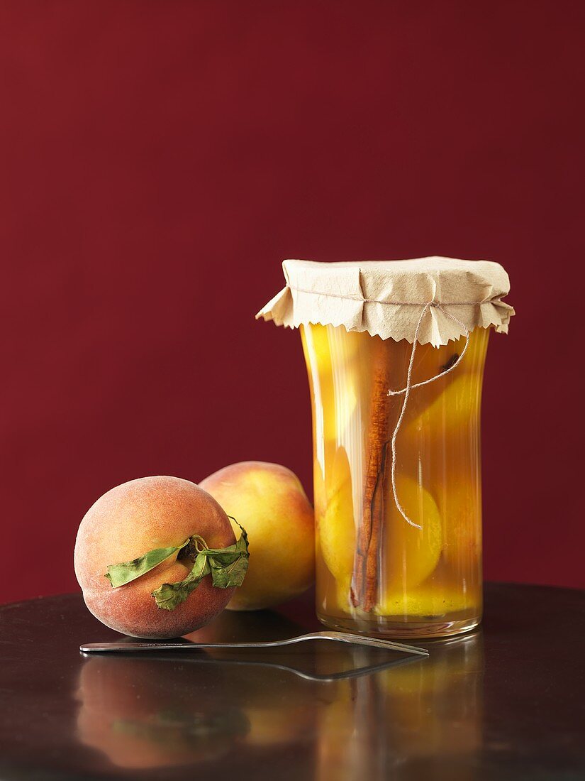 Jar of Homemade Pickled Peaches with Two Fresh Peaches