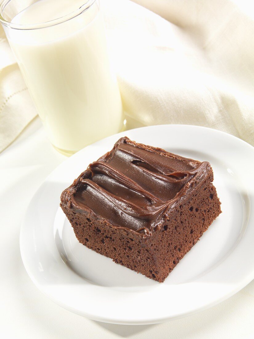 A Chocolate Brownie with Chocolate Frosting and a Glass of Milk