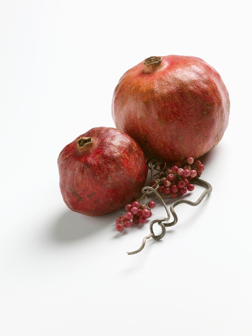 Two Pomegranates with Pepper Berries on White