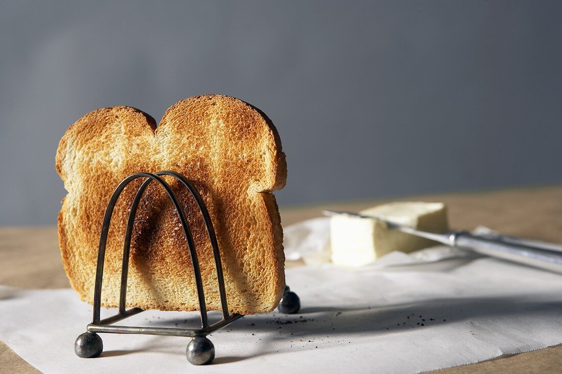 Toastscheibe im Toasthalter, Butter im Hintergrund