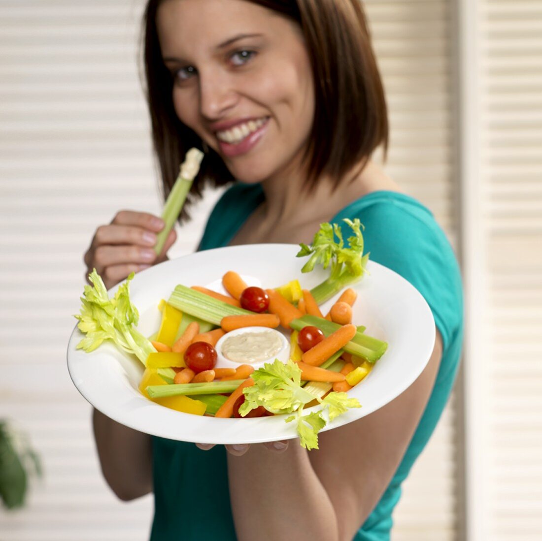 Woman Holding Vegetable Platter in One Hand and Celery in the Other