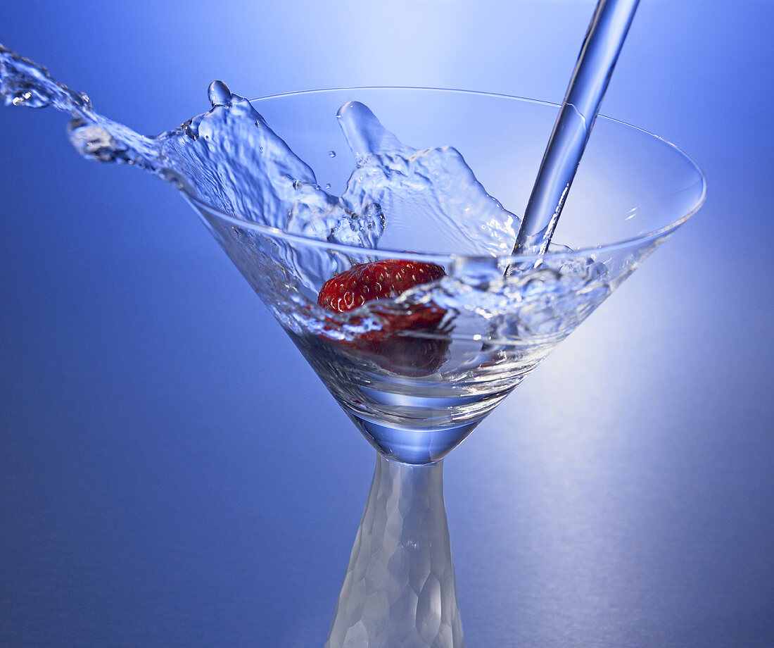 Martini in Glas mit Erdbeere eingiessen