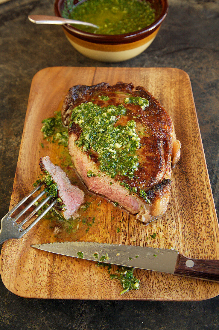 Rib Eye Steak with Herb Sauce on a Cutting Board, Knife and Fork