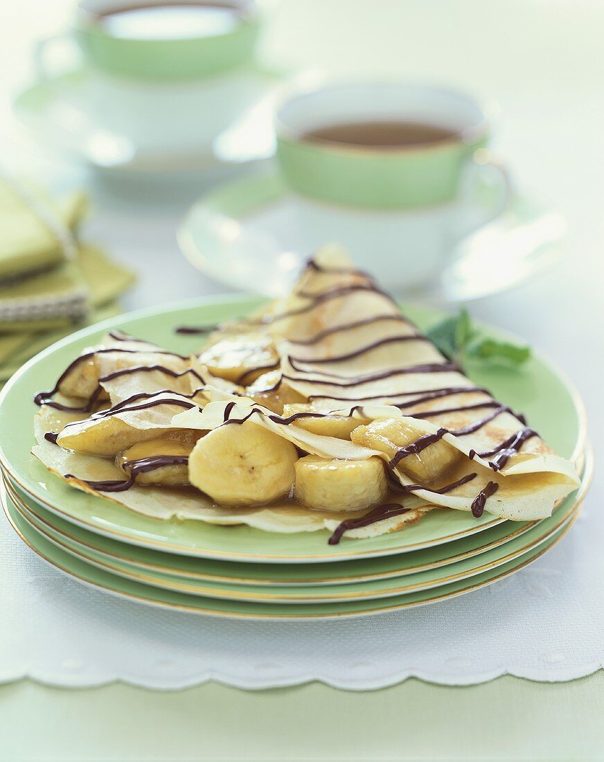 Banana Crepes with Chocolate Drizzles on a Stack of Green Plates