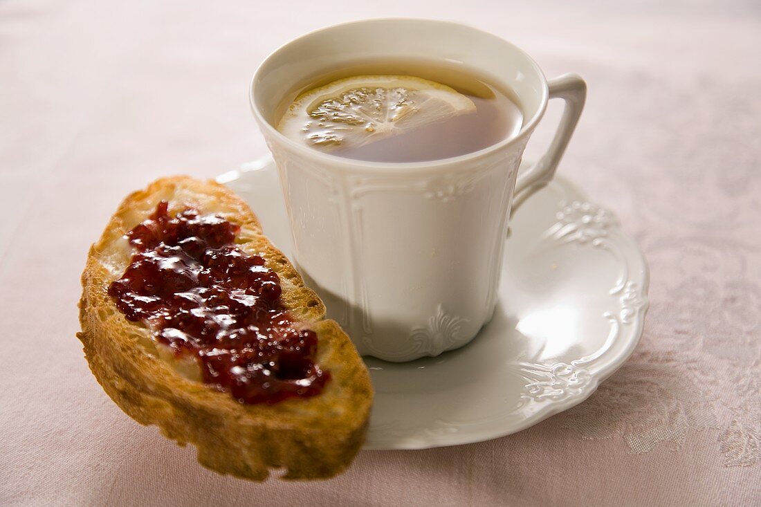 Eine Tasse Tee mit Zitrone und eine Scheibe Weißbrot mit Marmelade