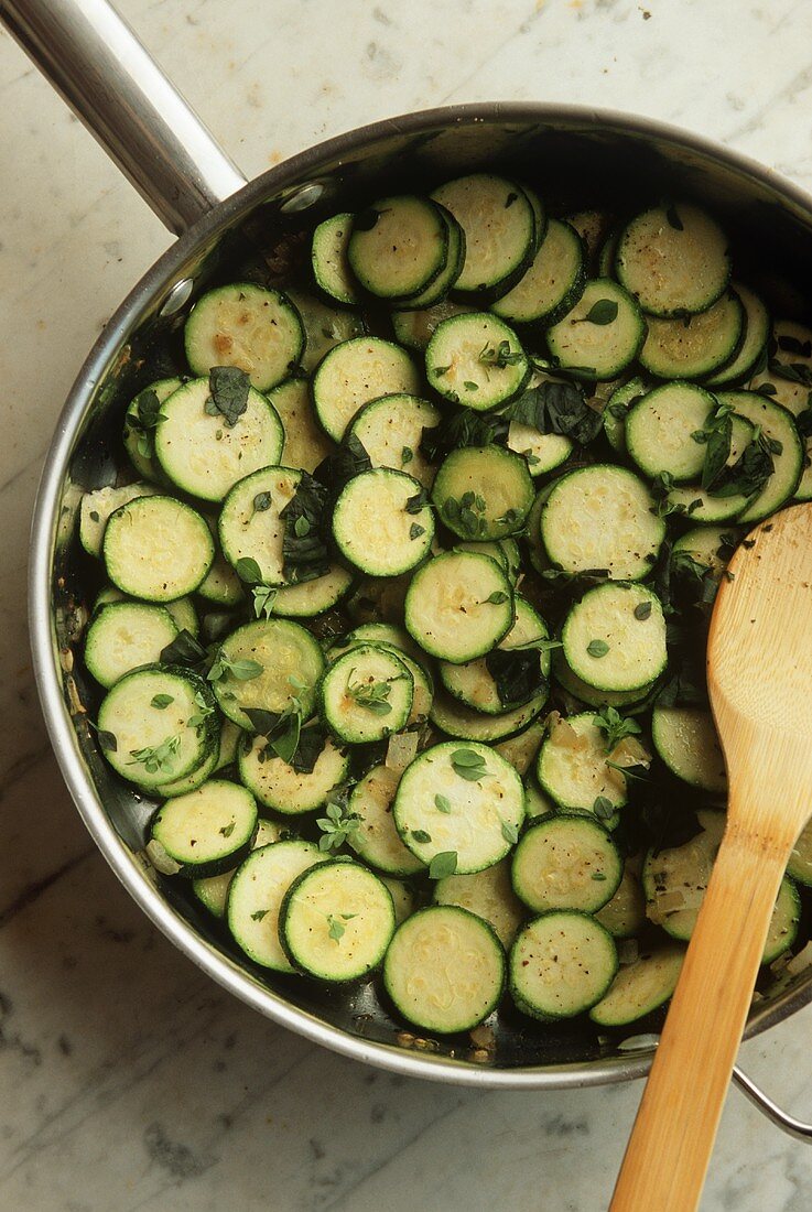 Sliced Sauteed Zucchini in a Skillet with a Wooden Spoon; From Above