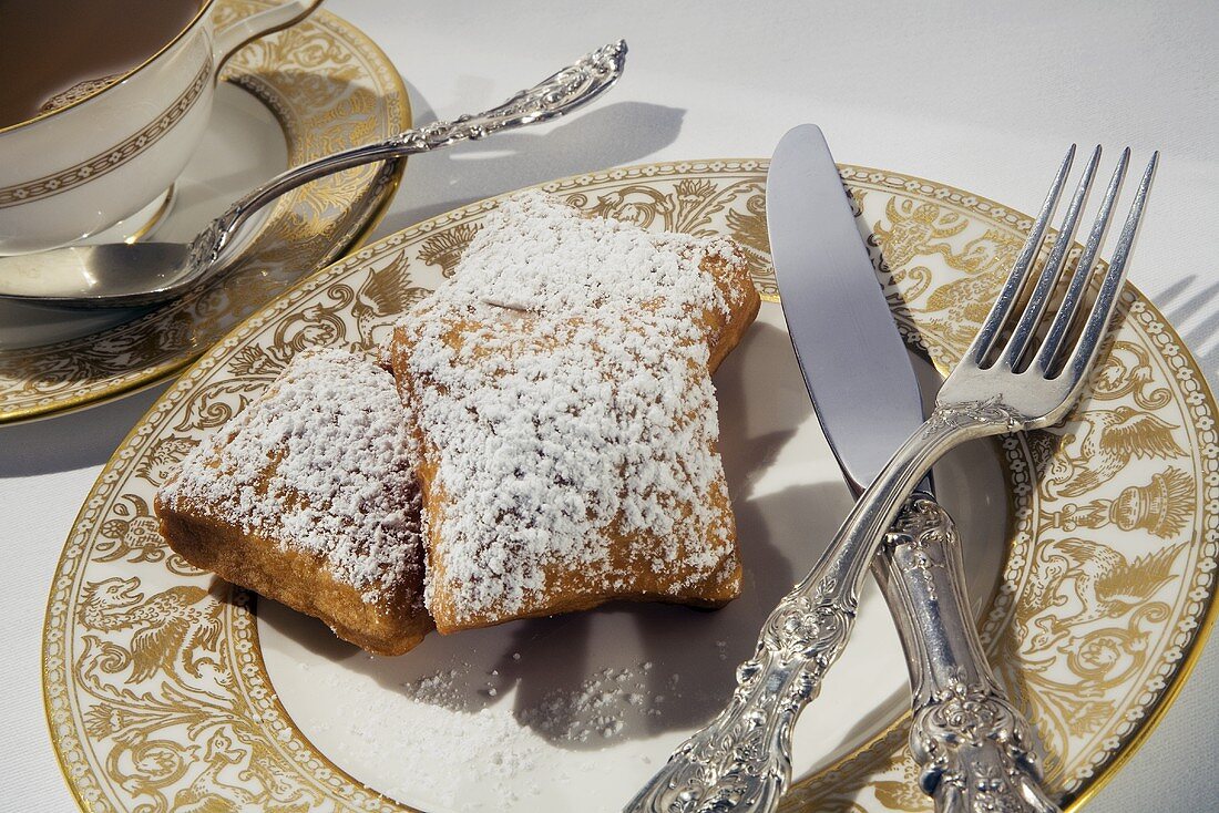Three Beignets Topped with Powdered Sugar on a Plate; Tea