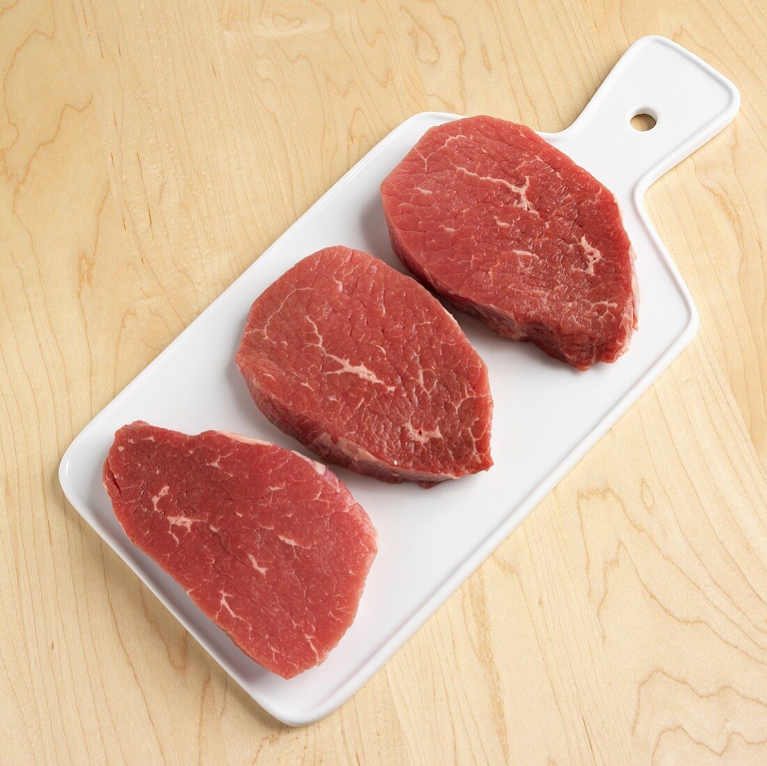 Three raw beef steaks on a chopping board