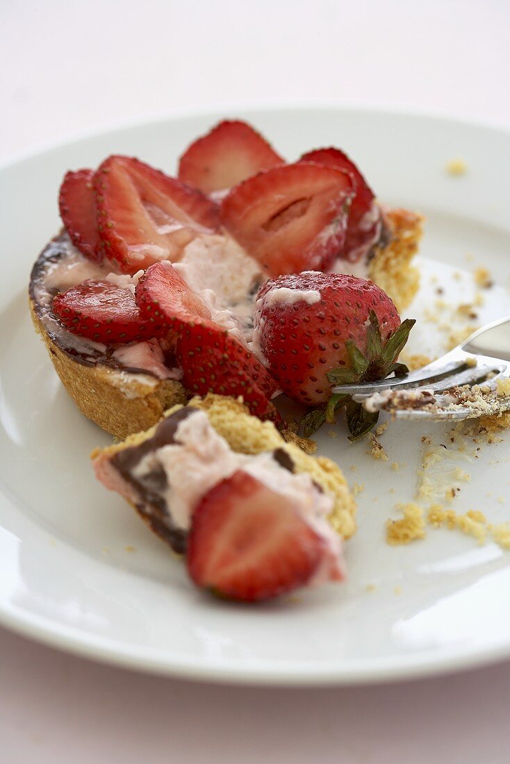 Angebissenes Erdbeer-Tortelett auf Teller mit Kuchengabel