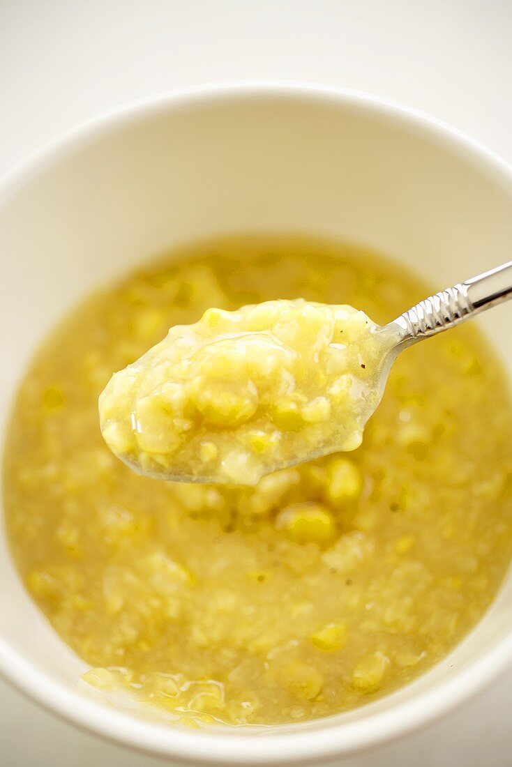Spoonful of Creamed Corn Over Bowl of Creamed Corn; Close Up