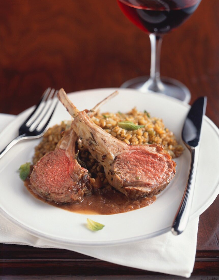 Rack of Lamb; Two Chops with Rice on a White Plate with a Fork and Knife