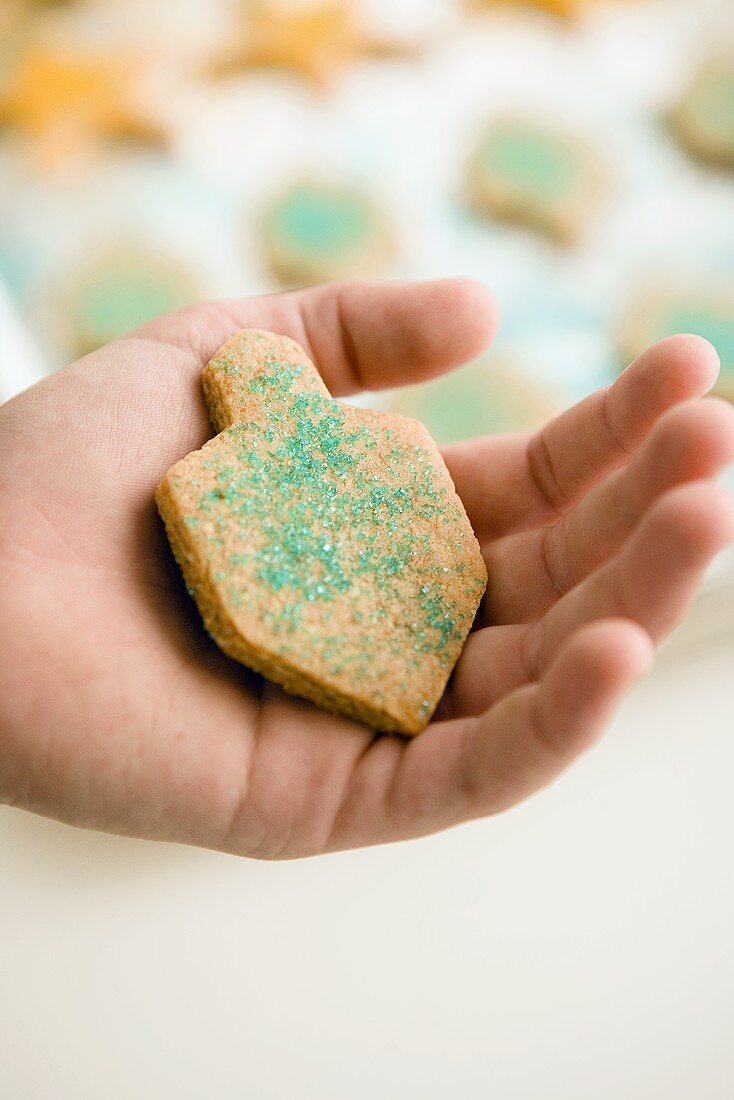 A hand holding a dreidel-shaped biscuit decorated with blue sprinkles
