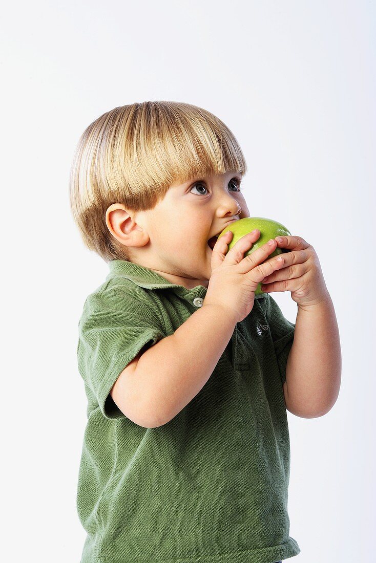 Ein kleiner Junge beisst in einen Granny Smith Apfel