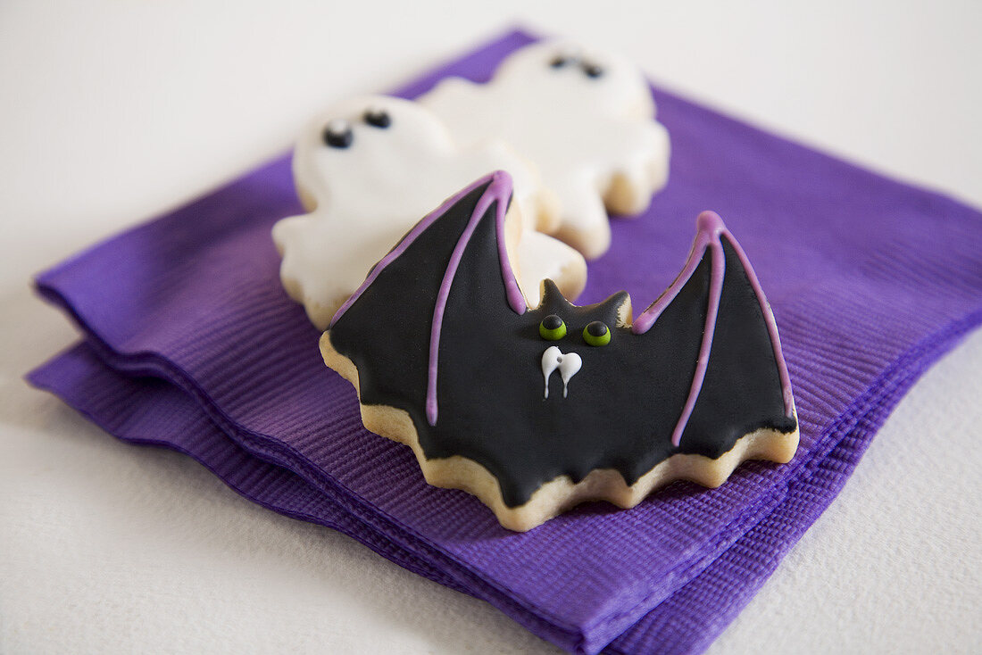 A Bat Cookie and Two Ghost Cookies on Purple Napkins for Halloween
