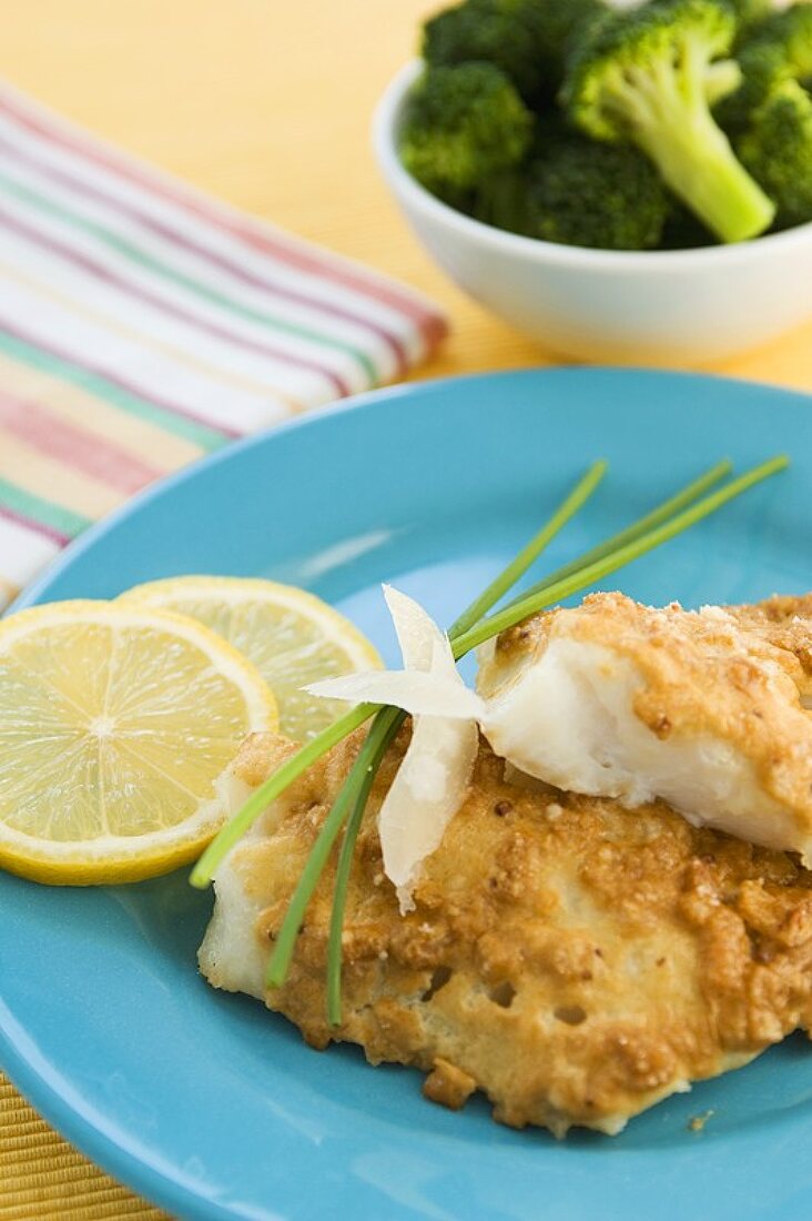 Fried White Fish Fillets on a Plate with Lemon Slices and Chives