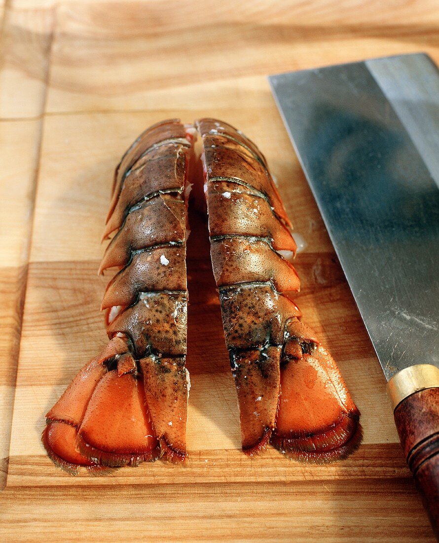 Lobster Tail Halved on a Cutting Board; Knife