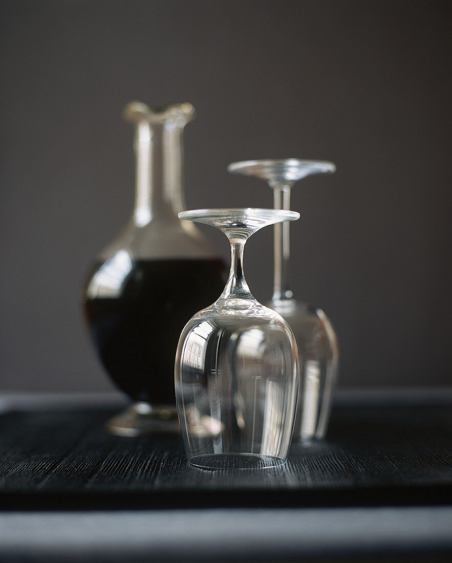 Two Empty Wine Glasses Turned Upside Down; Carafe of Red Wine