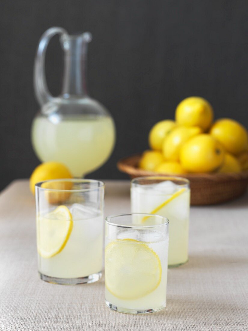 Zitronenlimonade in drei Gläsern mit Eiswürfeln und Karaffe