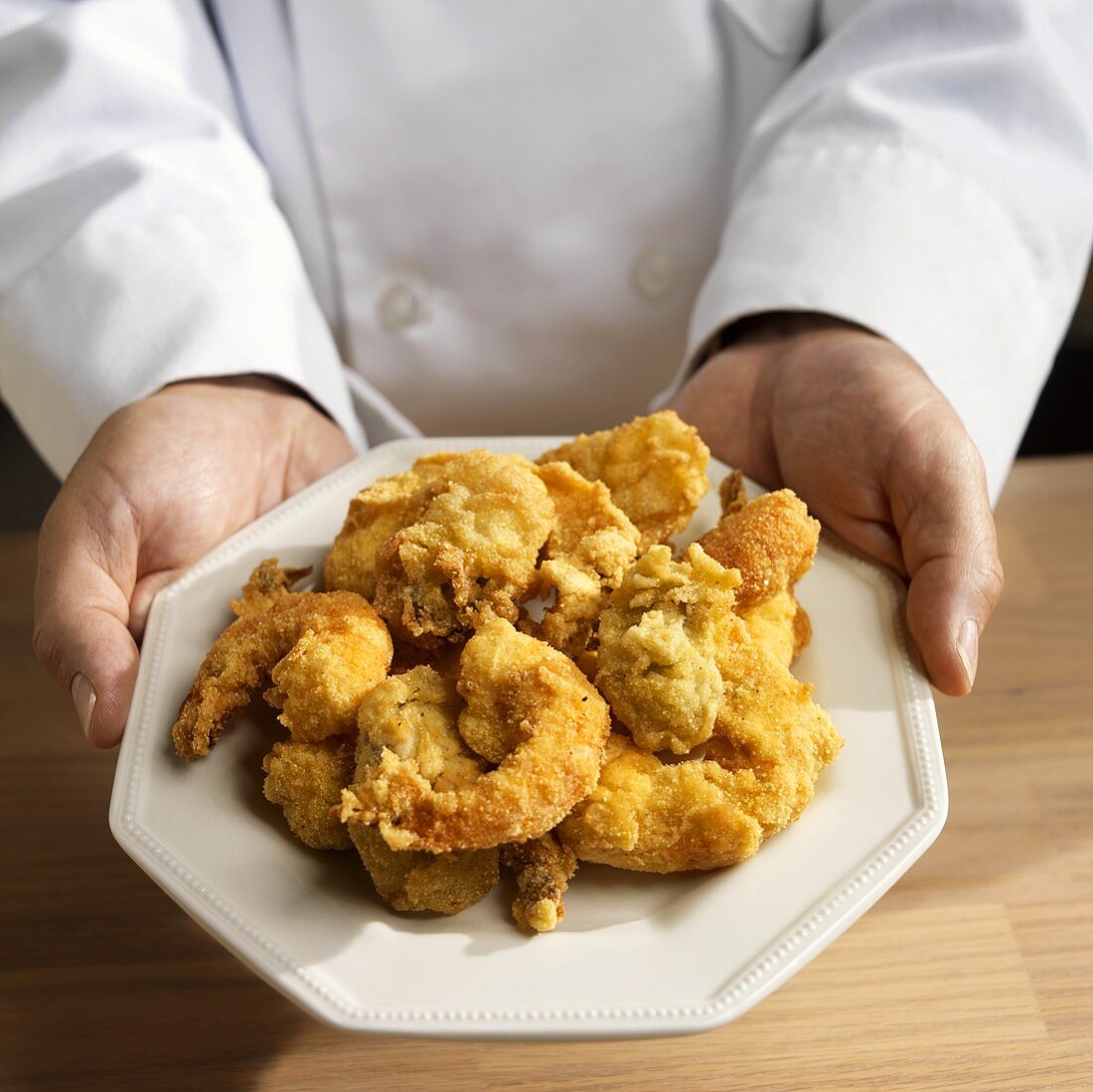 Koch hält Teller mit frittierten Shrimps und Austern