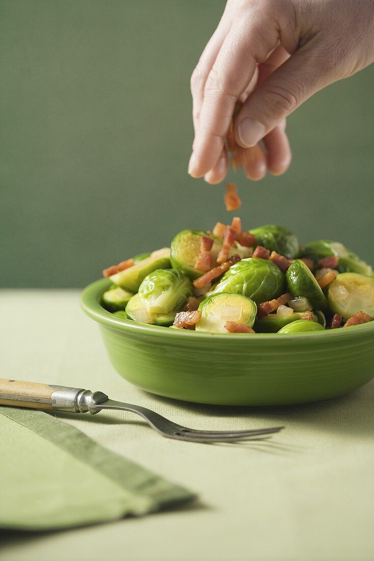 Hand Sprinkling Bacon Bits Over Brussles Sprouts