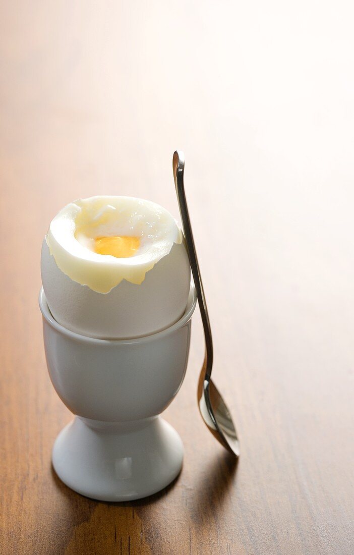 Weichgekochtes Ei im Eierbecher, daneben Löffel