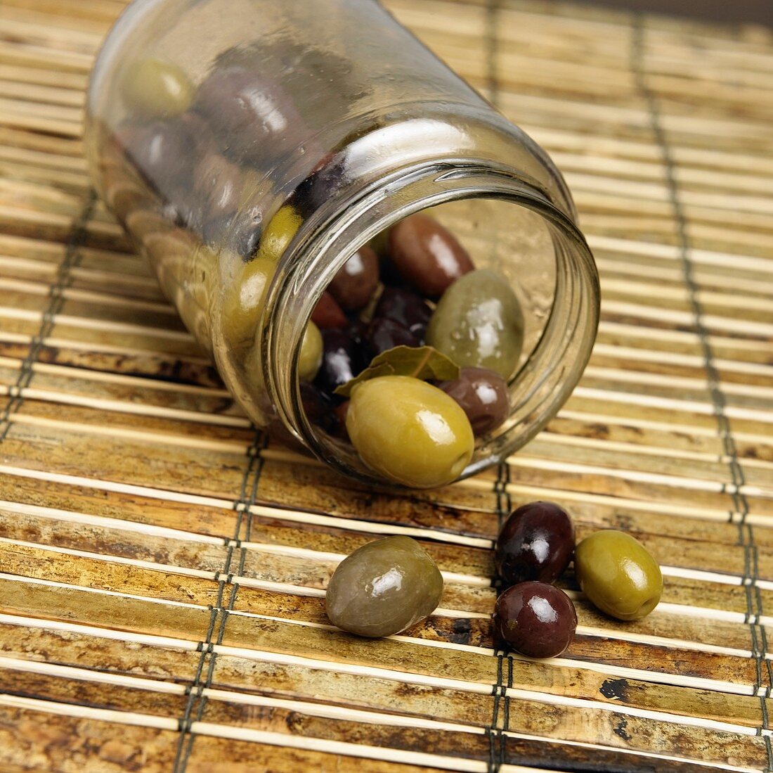 Umgekipptes Einweckglas eingelegter Oliven auf Bambusmatte