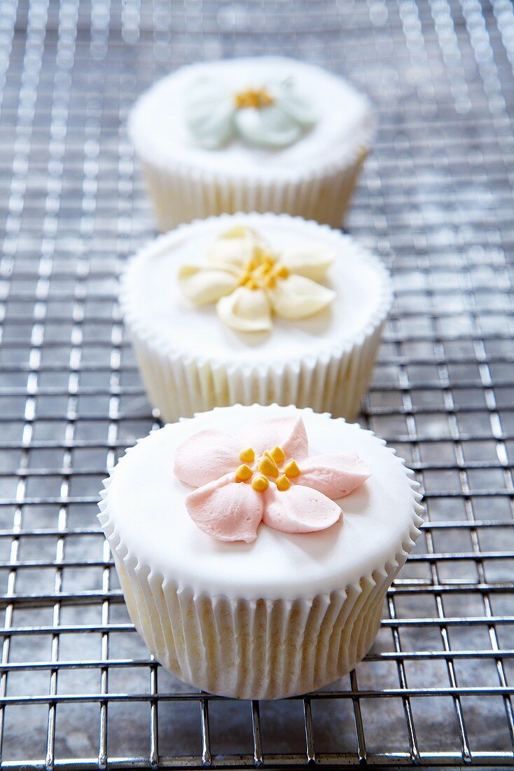 Three Cupcakes with Frosting Flowers on a Cooling Rack