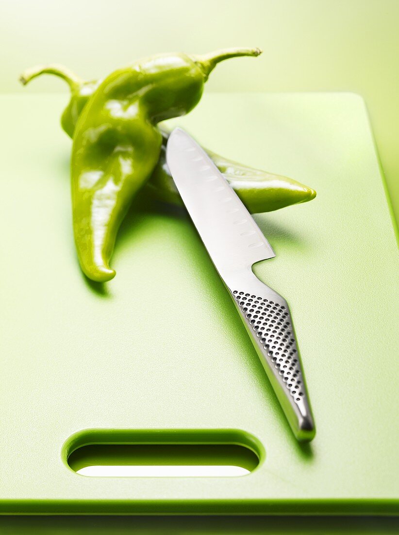 Zwei grüne Chilischoten mit Messer auf einem Schneidebrett