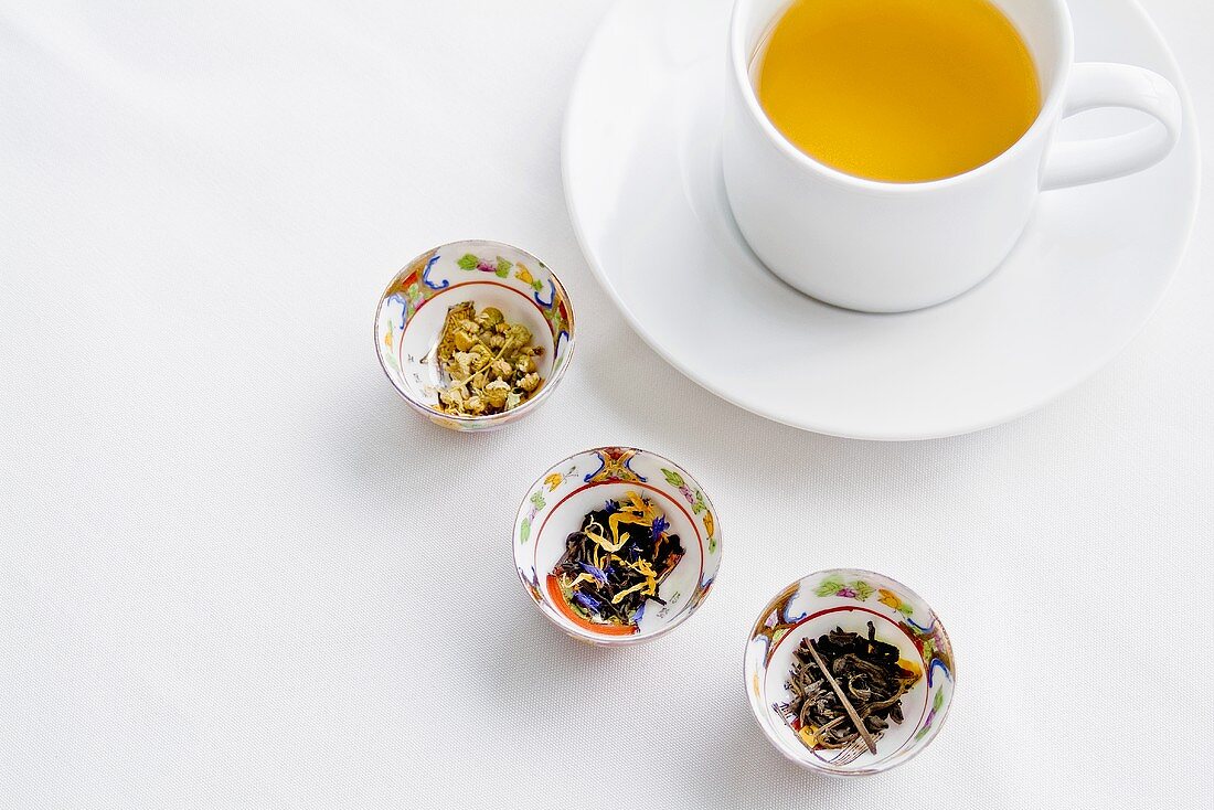 Drei Schälchen mit exotischen Teeblättern und eine Tasse Tee