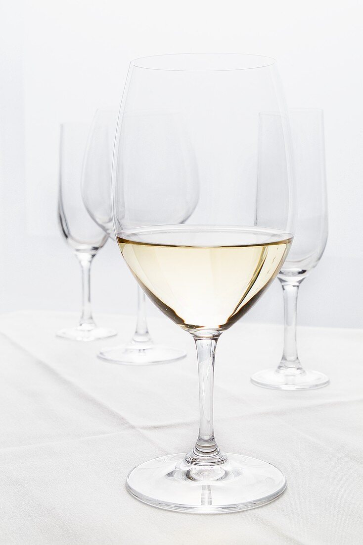 Ein Glas Weißwein, dahinter leere Gläser
