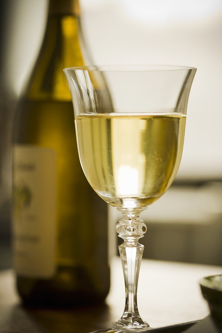 Ein Glas Weißwein, im Hintergrund Weissweinflasche