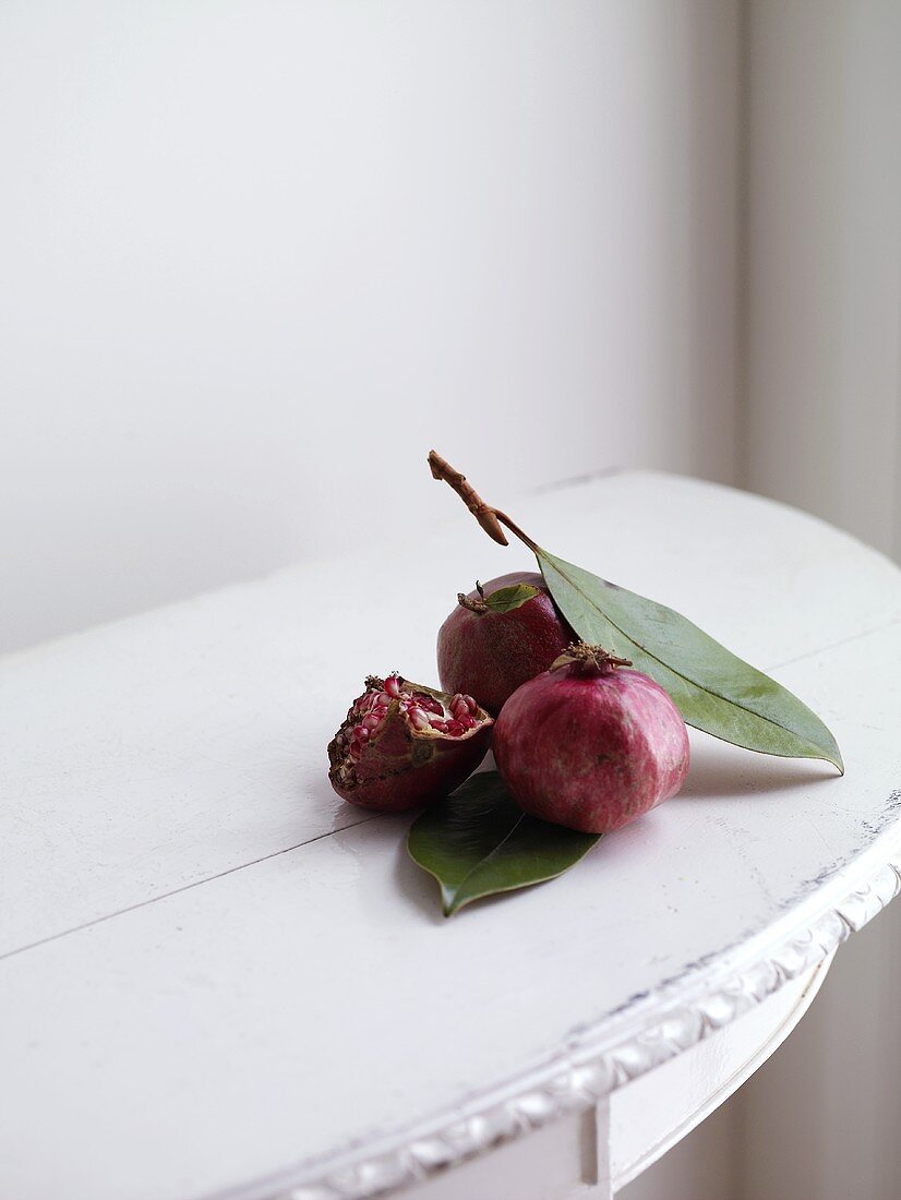 Granatäpfel mit Blättern auf kleinem Holztisch