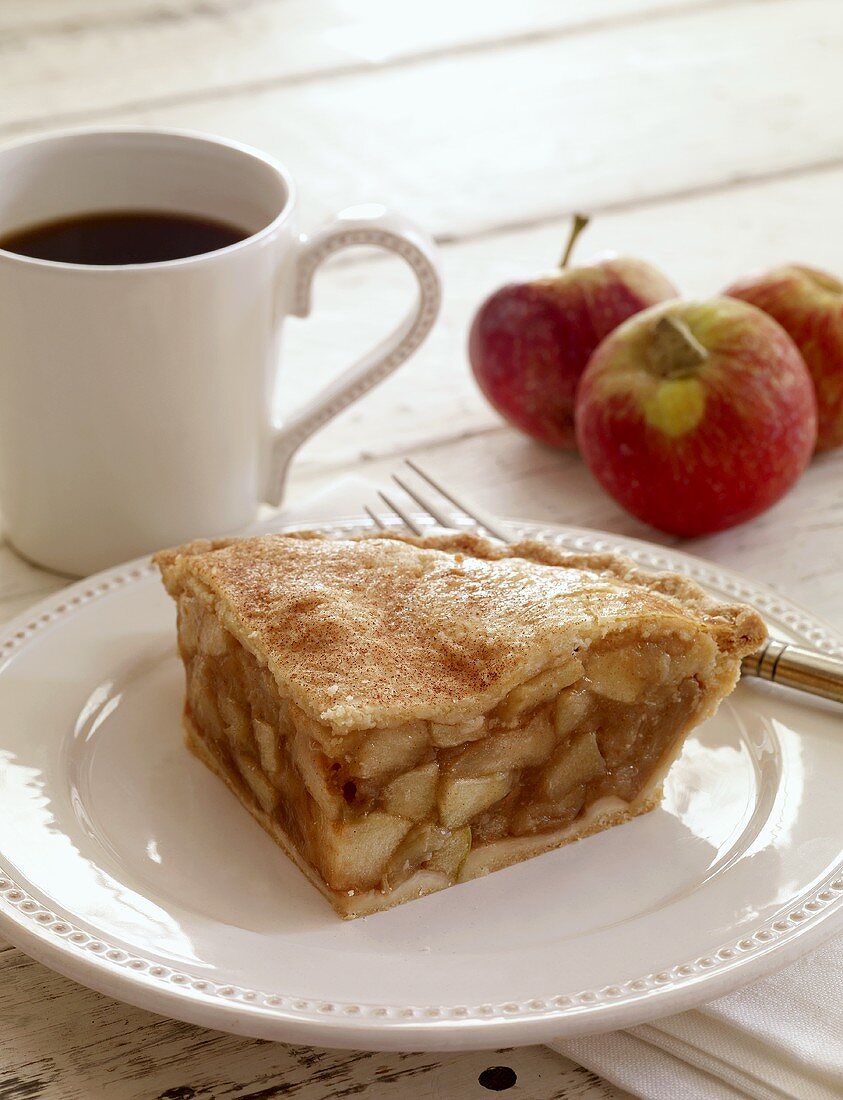 Ein Stück Applepie, Kaffeebecher und frische Äpfel