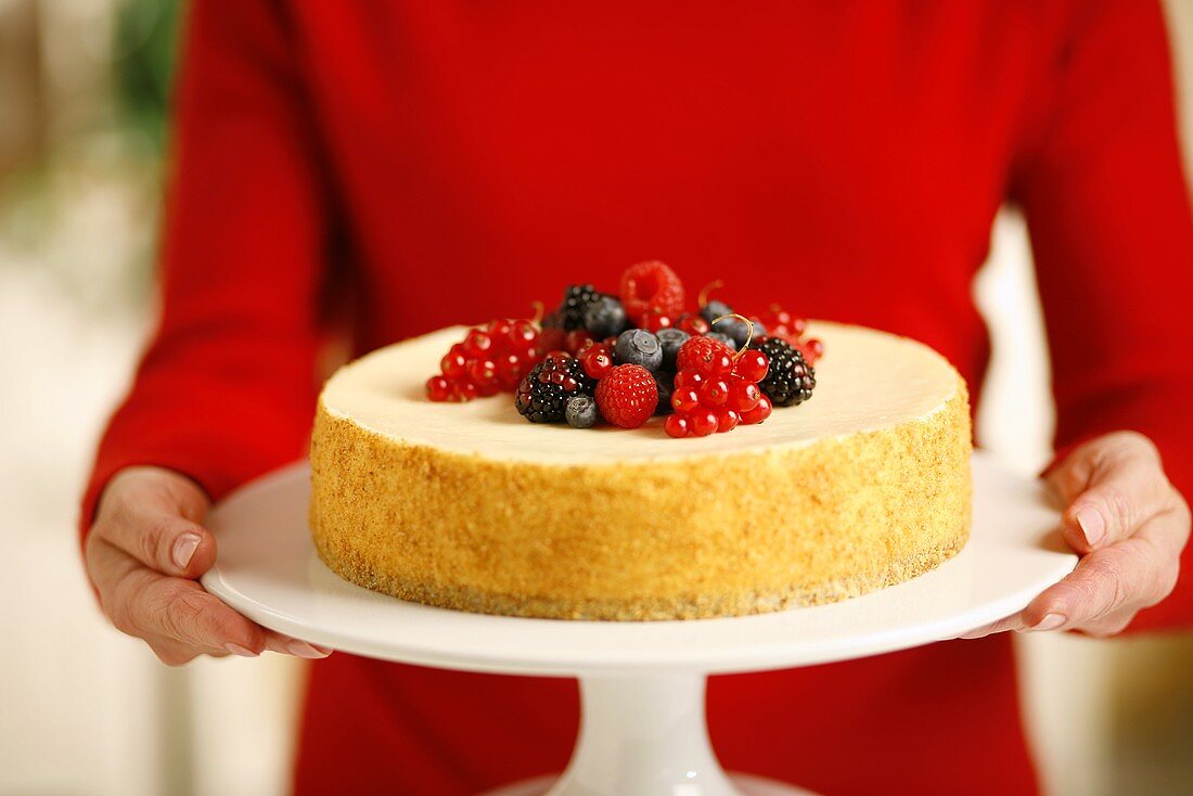 Frau hält Käsekuchen mit frischen Beeren