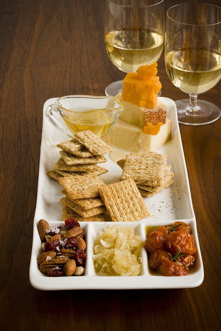 Platte mit Crackern, Käse und Nüssen, Weissweingläser