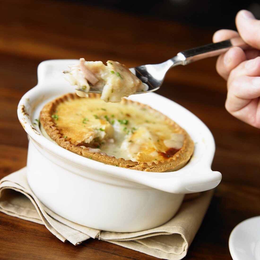 Hand Holding Fork with Chicken Pot Pie in Front of Whole Pie