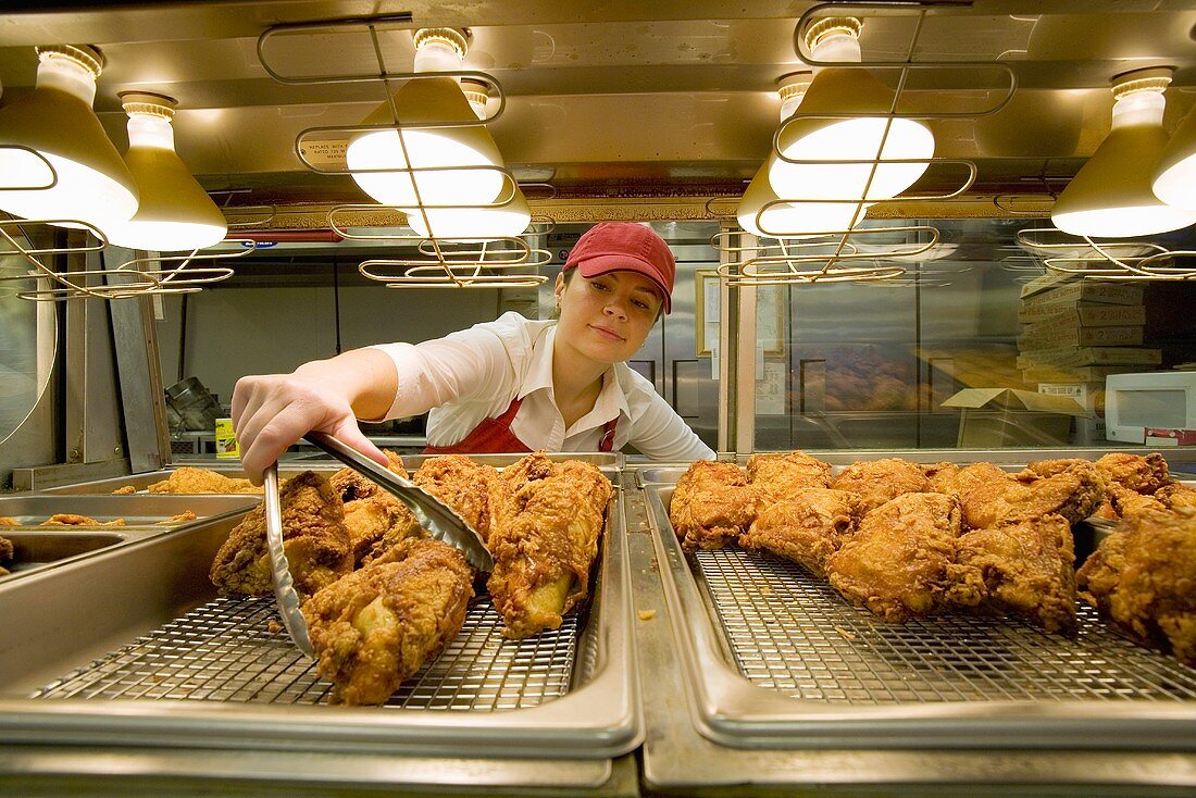 Woman Selecting Piece of Fried Chicken  From Under Heat Lamps