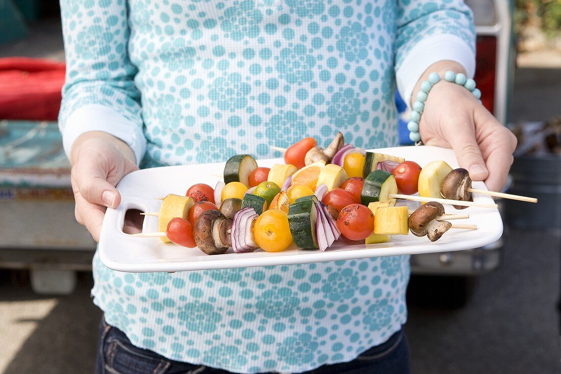 Frau hält Platte mit Gemüse-Obst-Spiessen