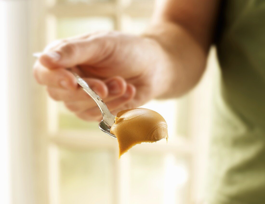 Man Holding a Spoonful of Creamy Peanut Butter