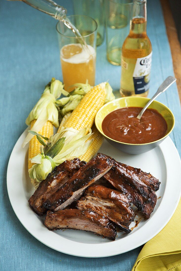 Gegrillte Spareribs mit Sauce und Maiskolben auf Teller, Bier