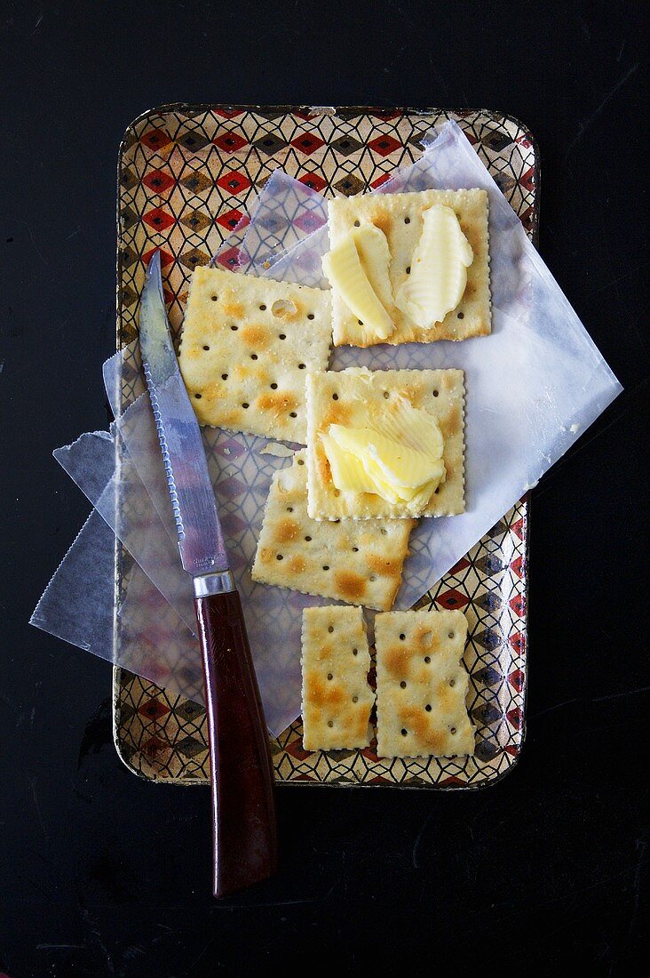 Cracker mit Butter und Messer auf Tablett