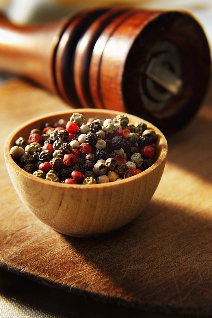 Red, Green, White and Black Peppercorns in Wooden Bowl with Pepper Grinder
