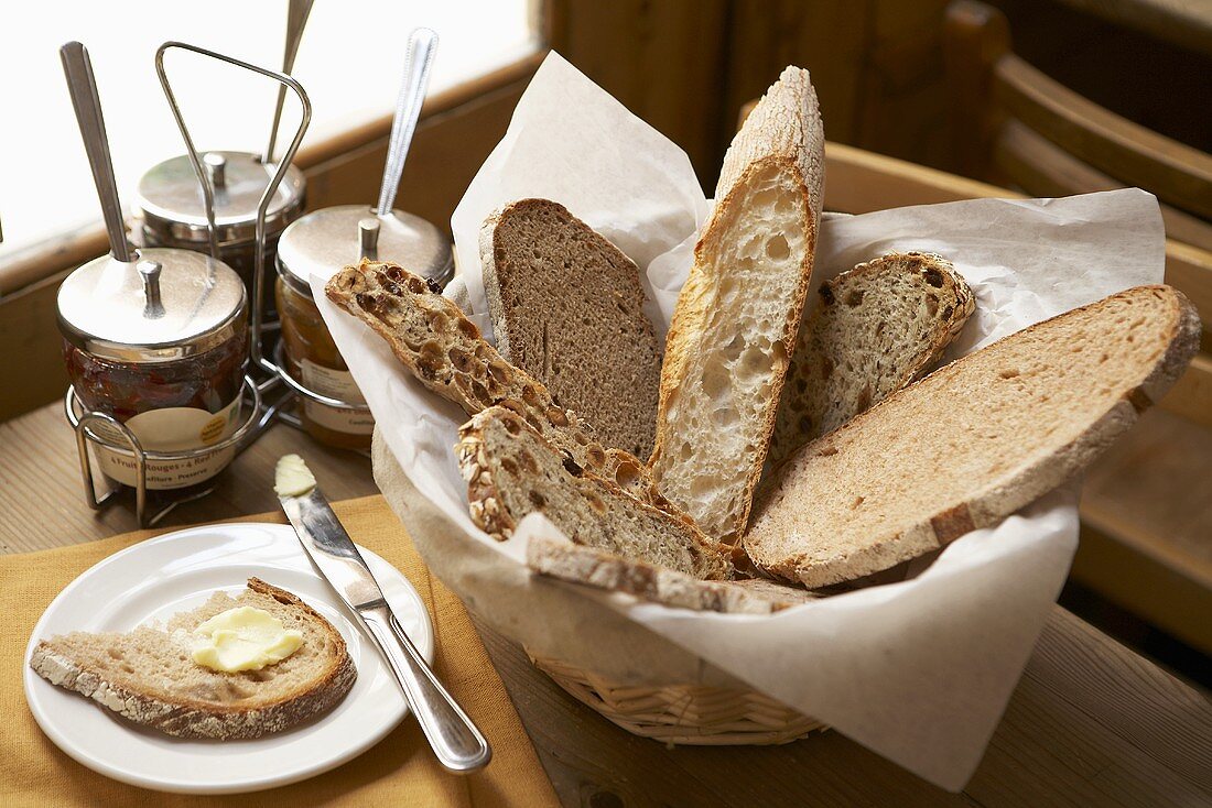 Verschiedene Brotscheiben im Brotkorb, Butterbrot und Marmeladengläser