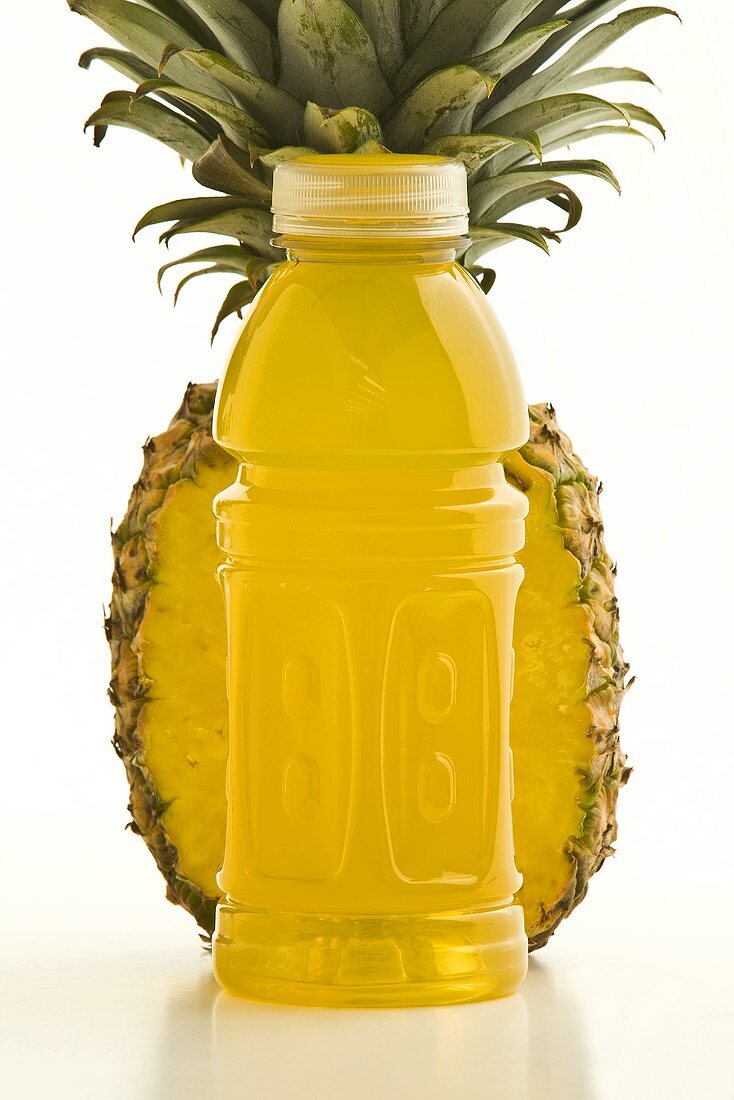Fitnessdrink in Plastikflasche vor halber Ananas