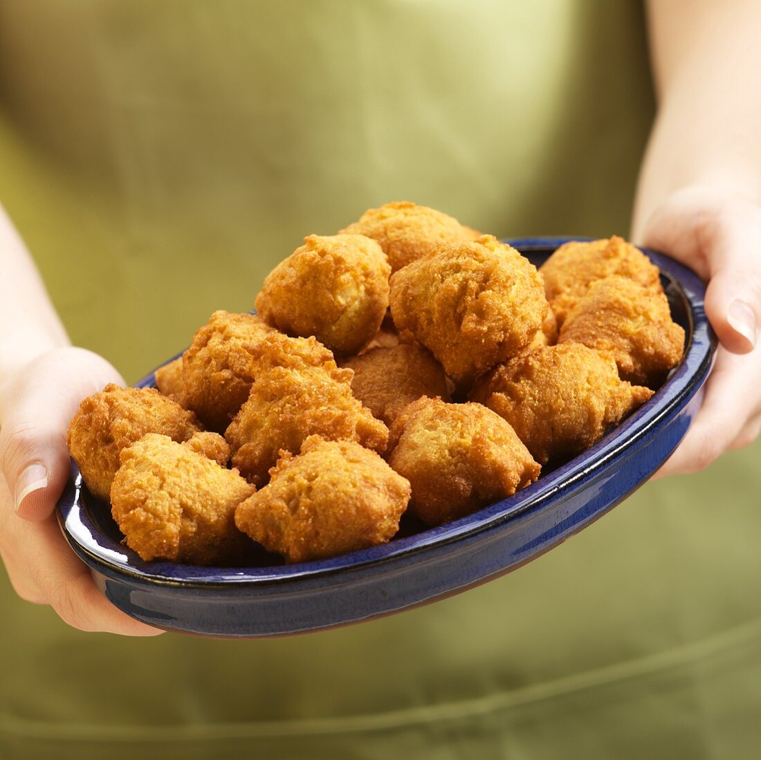 Hands Holding a Plate of Hush Puppies