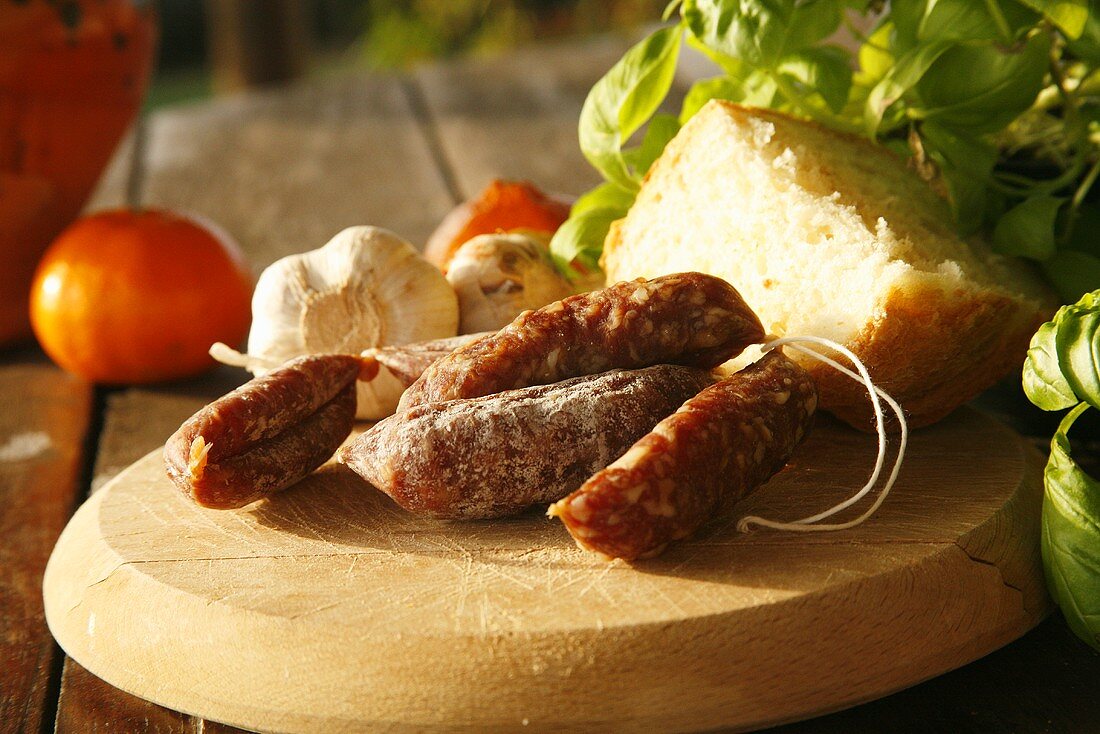 Cured Sausage Links on Cutting Board with Garlic, Bread and Basil