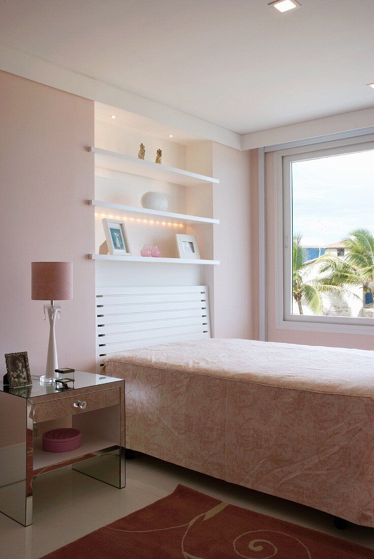 A bedroom with a single bed, a shelf above the bed in the wall niche and a bedside table